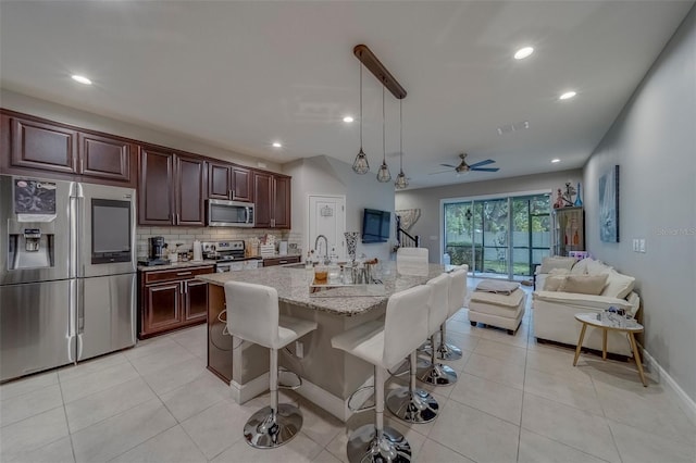 kitchen featuring light stone countertops, a breakfast bar area, tasteful backsplash, appliances with stainless steel finishes, and decorative light fixtures