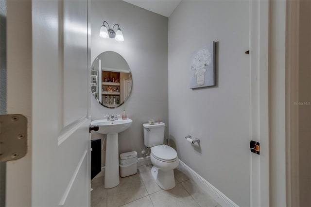 half bathroom featuring a sink, baseboards, tile patterned flooring, and toilet