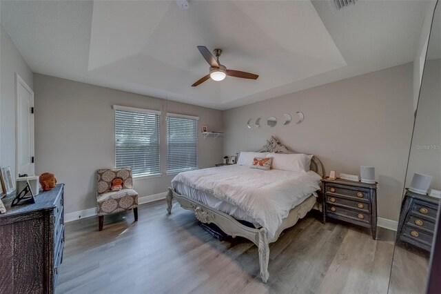 bedroom with ceiling fan, visible vents, wood finished floors, baseboards, and a raised ceiling