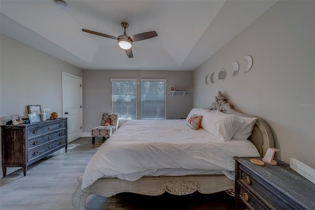 bedroom featuring a raised ceiling, a ceiling fan, and light wood-type flooring