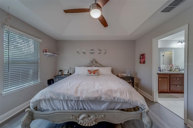 bedroom with visible vents, connected bathroom, a raised ceiling, a ceiling fan, and light wood-style flooring