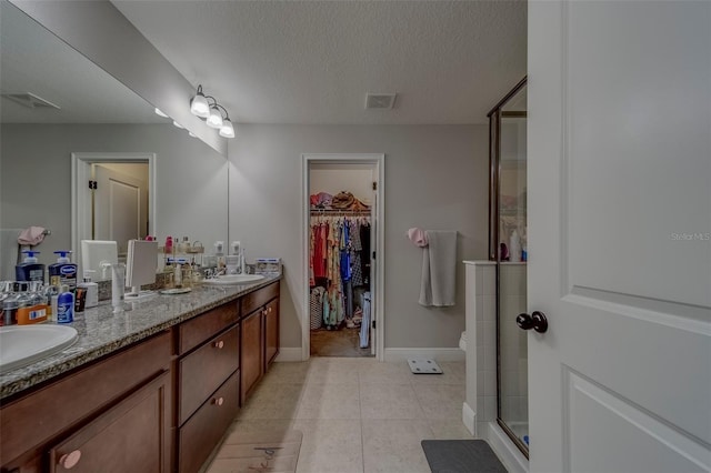 bathroom featuring visible vents, double vanity, a walk in closet, a shower stall, and a sink