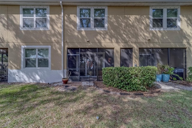 rear view of property featuring a lawn and stucco siding