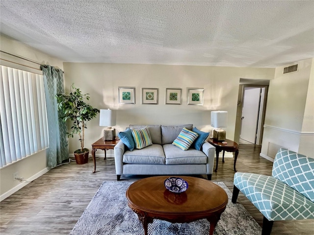 living area with wood finished floors, baseboards, a textured ceiling, and visible vents