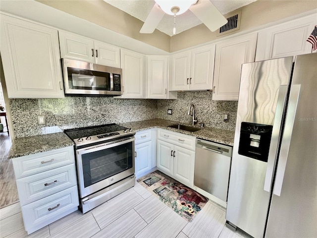 kitchen featuring visible vents, dark stone counters, white cabinets, a sink, and appliances with stainless steel finishes