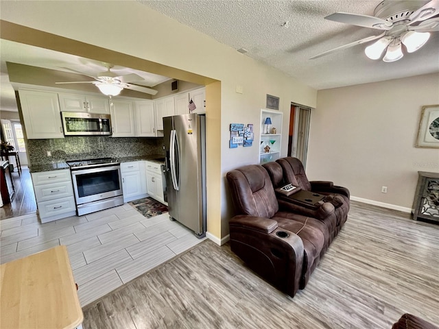 living room featuring light wood-style floors, baseboards, a ceiling fan, and a textured ceiling