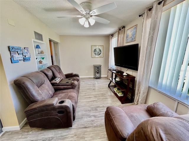 living area with light wood-style floors, baseboards, a ceiling fan, and a textured ceiling