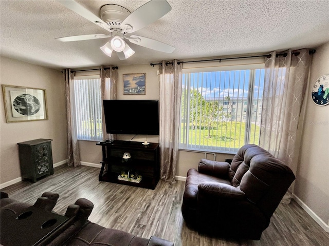 living room featuring baseboards, a ceiling fan, a textured ceiling, and wood finished floors