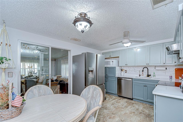 kitchen featuring wall chimney range hood, a textured ceiling, appliances with stainless steel finishes, a sink, and light countertops