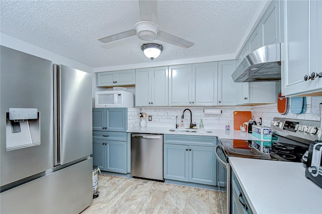 kitchen with a textured ceiling, a sink, light countertops, under cabinet range hood, and stainless steel appliances