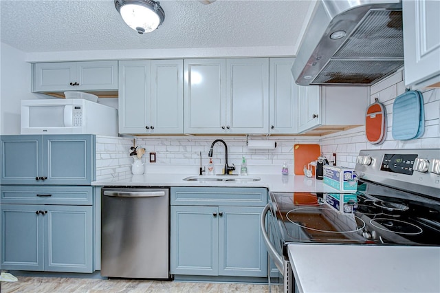 kitchen with decorative backsplash, wall chimney range hood, light countertops, a sink, and appliances with stainless steel finishes