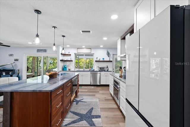 kitchen featuring stainless steel appliances, open shelves, healthy amount of natural light, light wood-style flooring, and a textured ceiling
