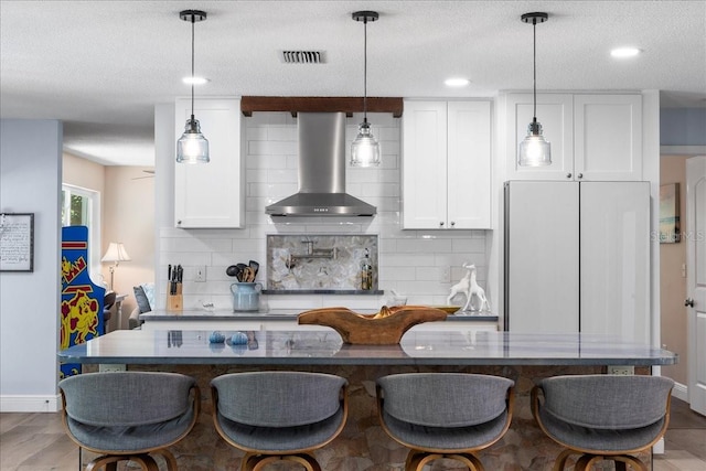 kitchen featuring wall chimney exhaust hood, white cabinetry, tasteful backsplash, decorative light fixtures, and a textured ceiling