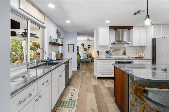 kitchen featuring wall chimney range hood, a sink, a ceiling fan, appliances with stainless steel finishes, and backsplash