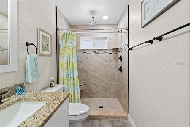 bathroom with a stall shower, toilet, wood finished floors, vanity, and a textured wall