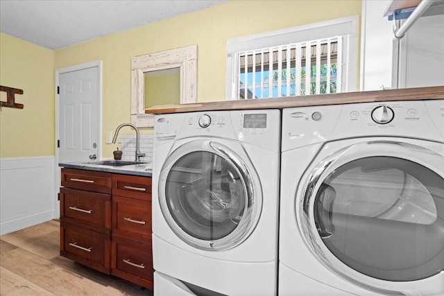 laundry area featuring washer and clothes dryer, light wood-style floors, wainscoting, cabinet space, and a textured ceiling