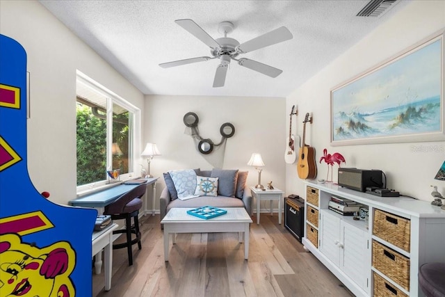 living area featuring light wood finished floors, ceiling fan, and a textured ceiling