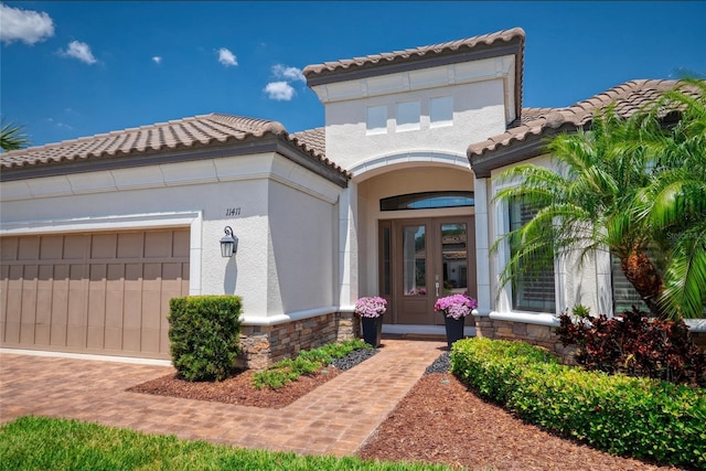 doorway to property featuring a garage, a tiled roof, stucco siding, and stone siding