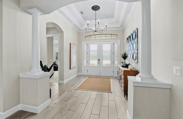 entrance foyer featuring arched walkways, light wood-type flooring, ornamental molding, a tray ceiling, and ornate columns