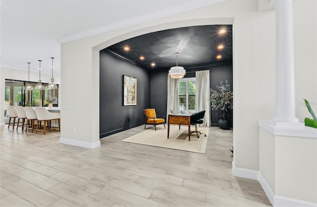 interior space featuring ornate columns, light wood finished floors, crown molding, and baseboards