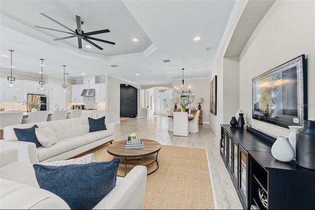living area featuring ornamental molding, recessed lighting, a raised ceiling, light wood-style flooring, and ceiling fan with notable chandelier