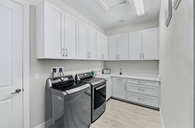 laundry room featuring light wood-style floors, visible vents, cabinet space, and washer and clothes dryer