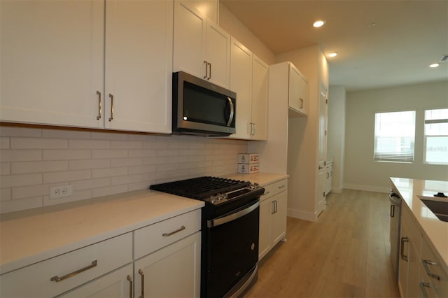 kitchen featuring tasteful backsplash, light wood-type flooring, gas stove, stainless steel microwave, and white cabinetry