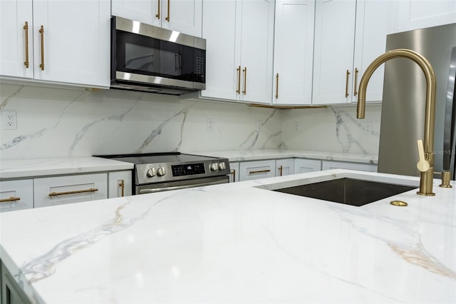 12484 Cross St, Largo, FL 33773 - kitchen featuring appliances with stainless steel finishes, backsplash, light stone countertops, and white cabinetry
