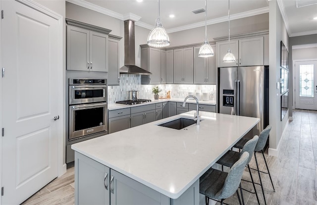 kitchen with gray cabinets, a kitchen bar, tasteful backsplash, a sink, and wall chimney exhaust hood