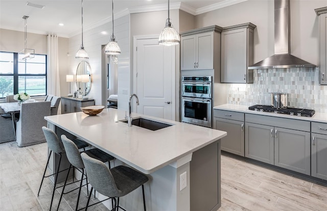 kitchen with wall chimney range hood, gray cabinets, and a sink