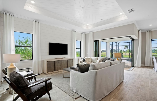 living area featuring light wood-style flooring, recessed lighting, a tray ceiling, visible vents, and ornamental molding