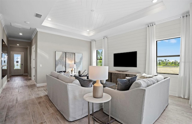 living room featuring light wood finished floors, baseboards, a tray ceiling, visible vents, and ornamental molding