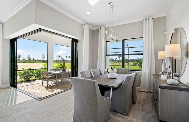 dining room with ornamental molding, light wood finished floors, golf course view, and a notable chandelier