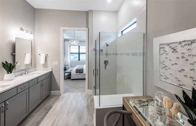 ensuite bathroom featuring double vanity, wood finished floors, baseboards, ensuite bathroom, and tiled shower