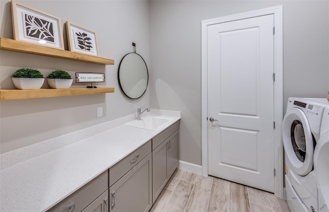 laundry area with washing machine and dryer, cabinet space, a sink, baseboards, and light wood finished floors