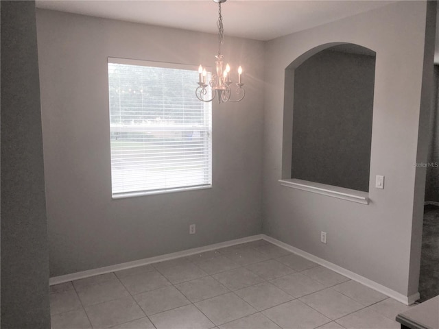 unfurnished room with an inviting chandelier, arched walkways, baseboards, and light tile patterned floors
