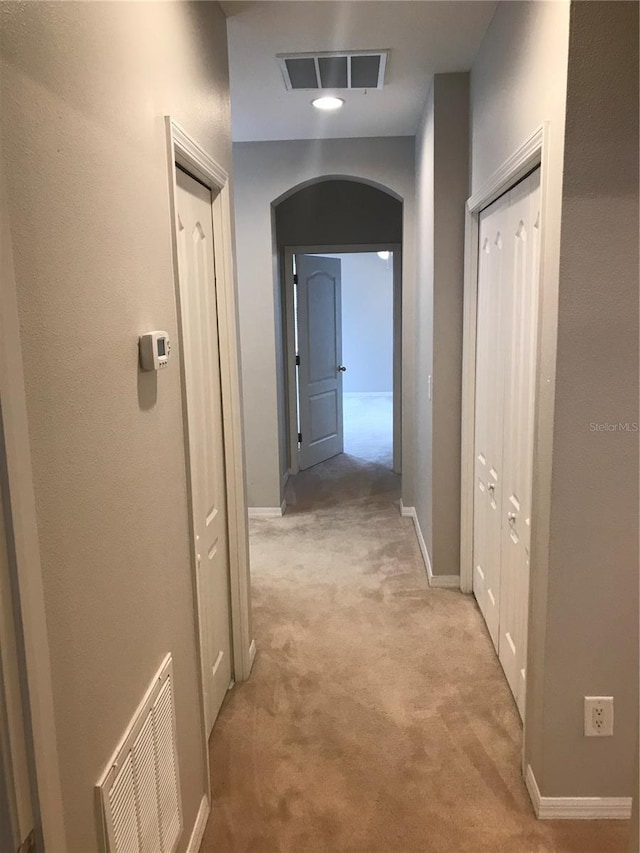 corridor with arched walkways, light colored carpet, visible vents, and baseboards
