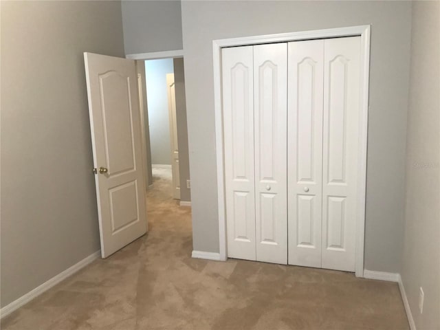 unfurnished bedroom featuring baseboards, a closet, and light colored carpet