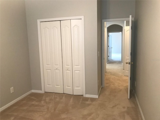unfurnished bedroom with baseboards, light carpet, a closet, and arched walkways