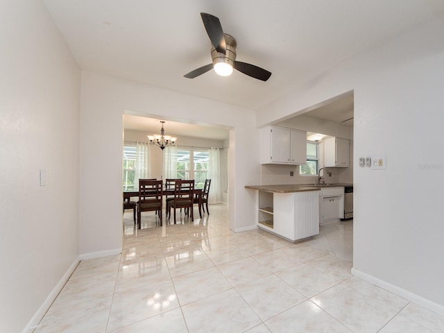 kitchen featuring dark countertops, baseboards, a sink, ceiling fan with notable chandelier, and light tile patterned floors