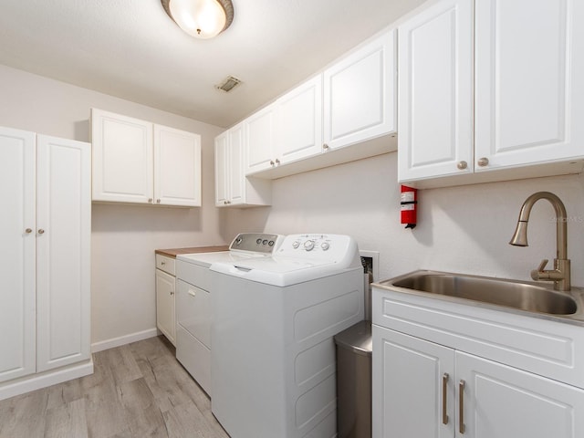 washroom with visible vents, cabinet space, separate washer and dryer, a sink, and light wood-style flooring