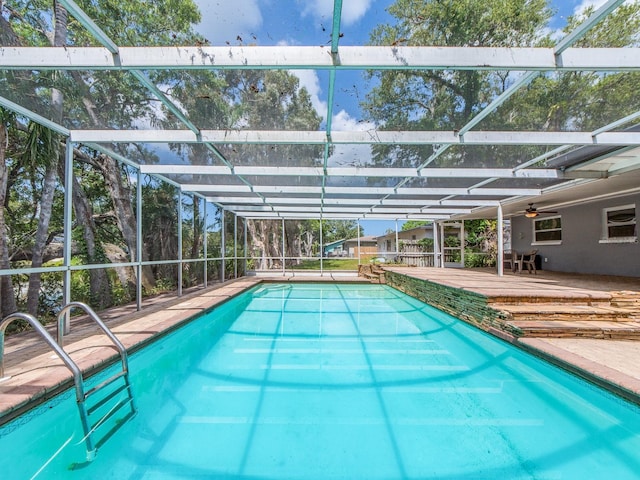 outdoor pool with glass enclosure, a ceiling fan, and a patio area
