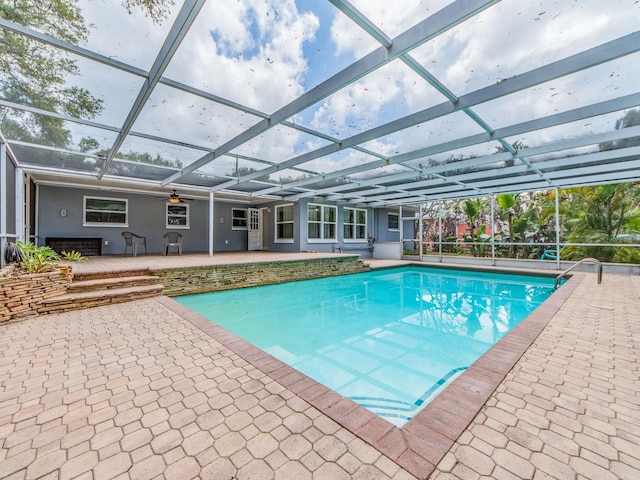 outdoor pool featuring glass enclosure, ceiling fan, and a patio area