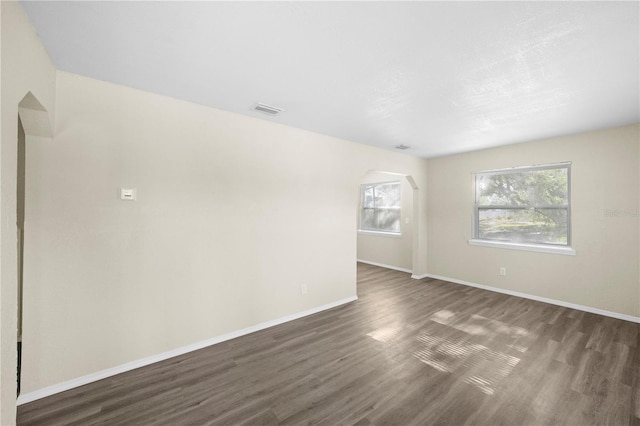 spare room featuring visible vents, baseboards, and dark wood-style floors