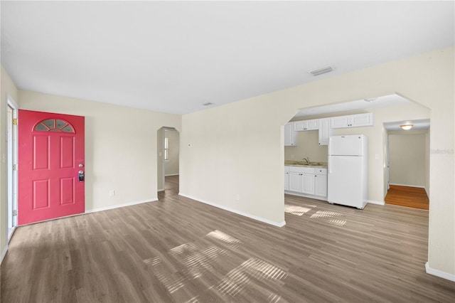 unfurnished living room with wood finished floors, baseboards, arched walkways, and a sink