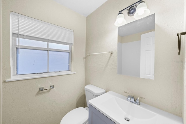 bathroom featuring toilet, vanity, and a textured wall