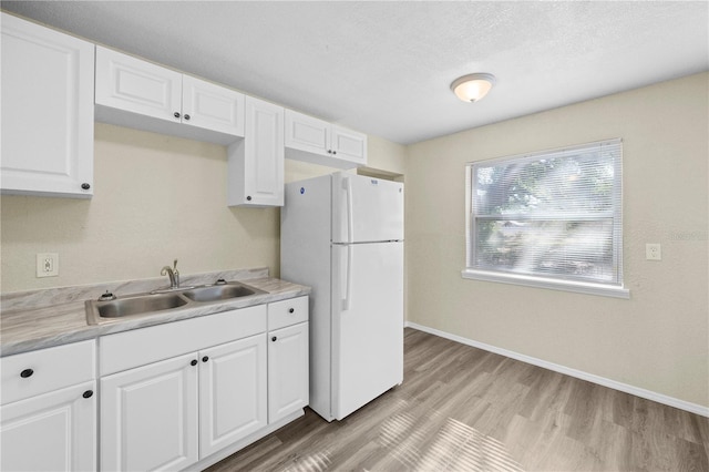 kitchen with a sink, freestanding refrigerator, white cabinetry, light countertops, and light wood-style floors