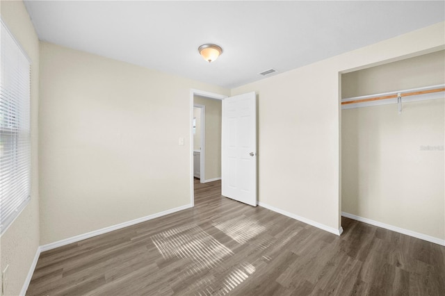 unfurnished bedroom with a closet, visible vents, wood finished floors, and baseboards