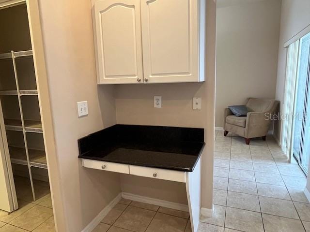 kitchen with dark countertops, baseboards, light tile patterned flooring, and white cabinetry