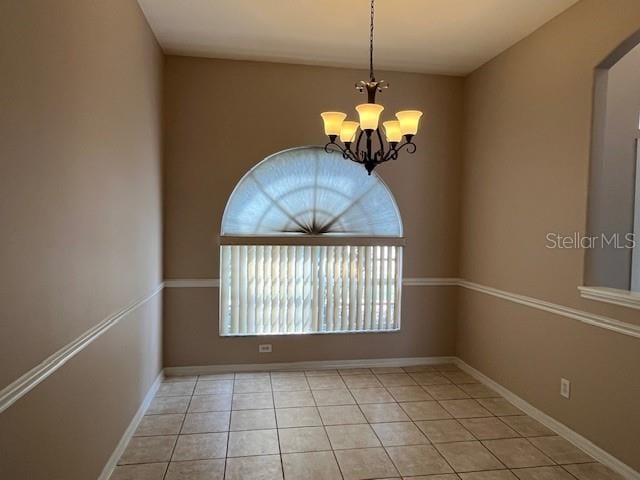 spare room featuring baseboards, light tile patterned floors, and a chandelier